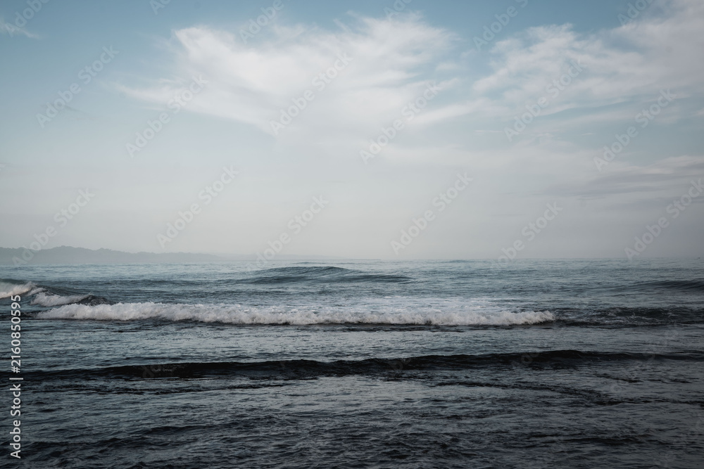 Obraz premium Moody coastal seascape with gentle waves, overcast sky and distant horizon, soft muted tones and textured ocean surface