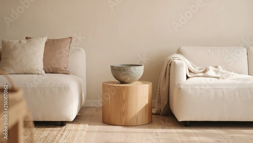 Minimalist living room interior showing two cream sofas beside a round wooden side table with separated cylindrical wooden displays serene living