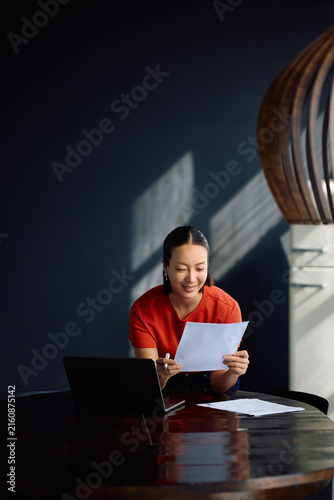 Happy Korean woman going through paperwork while working at home.
