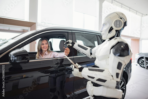 A futuristic robot interacts with a woman inside a car at a modern dealership, showcasing advanced technology in sales