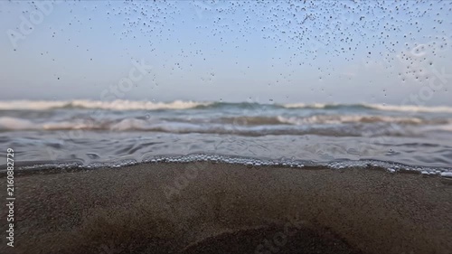 Long slow motion shot of sea waves at sunset with underwater bubbles droplets and water flowing across the camera lens