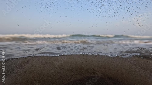 Long slow motion shot of sea waves at sunset with underwater bubbles droplets and water flowing across the camera lens