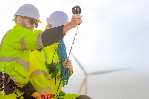 Принти на полотні A wind farm worker holds a vane anemometer high on its coiled lead so the impell