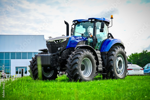 Modern blue tractor parked on green grass with an office building in the background. Clean agricultural machinery scene representing innovation and modern farming.