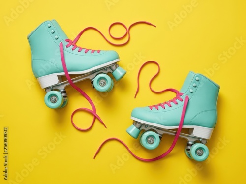 Two mint green roller skates with pink laces on a vibrant yellow background