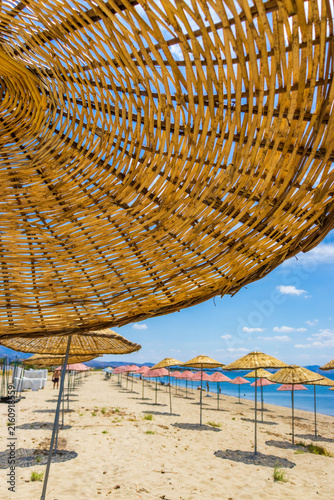 Sunny beach near cunda island on the aegean coast in turkey with straw umbrellas and turquoise sea. Travel, relaxation and summer vacation concept. 