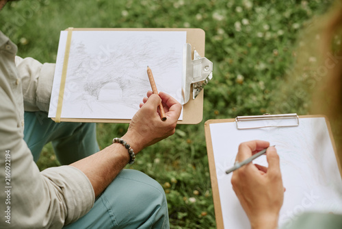 Unrecognizable young adults drawing on clipboards during outdoor art master class  practicing sketching skills. Image suitable for promoting creative workshops and recreational education