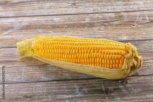 Foto Fresh yellow corn on cob with husk partially peeled on rustic wooden surface