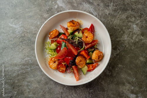 Shrimp salad with vegetables served in a white bowl on a gray table