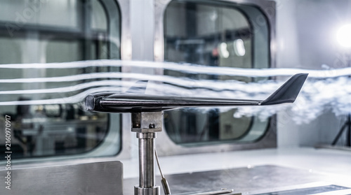 Carbon fiber airplane wing model mounted inside modern wind tunnel facility displaying white smoke trail airflow aerodynamics testing engineering laboratory research equipment