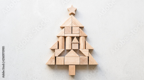 Flat lay arrangement featuring blank wooden building blocks shaped into festive holiday tree form topped with crafted star over light gray textured background surface
