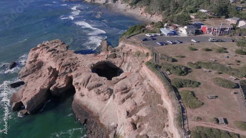 Aerial view of Thor's Well, a natural sinkhole in the rocky coastline with crashing waves and a nearby parking area in Oregon City, Oregon, United States.