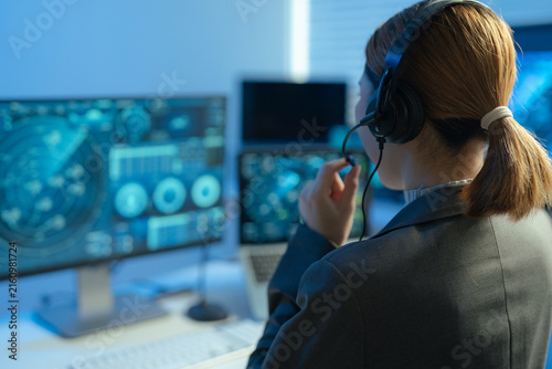 Female air traffic controller monitors flight radar screens in a modern dark command center, aviation technology, flight safety, surveillance and precision.