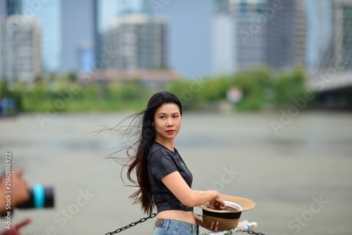 Young Asian woman with long hair blowing in the wind holding a straw hat during an outdoor city photo shoot