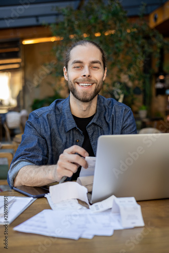 Happy business owner holding receipt near laptop