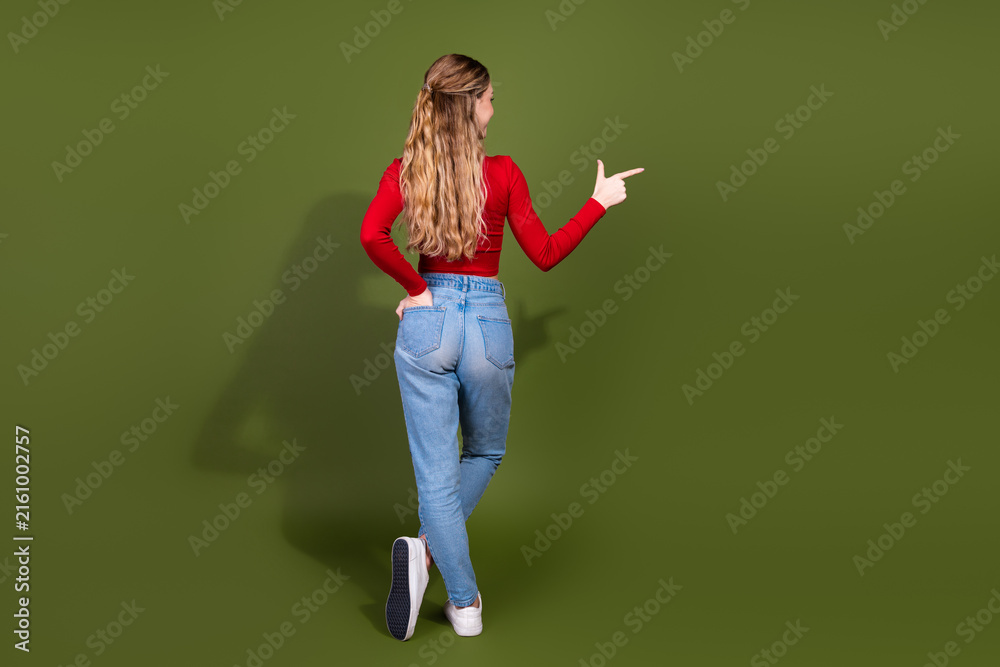 Naklejka premium Young woman in red top and jeans points with finger against green background