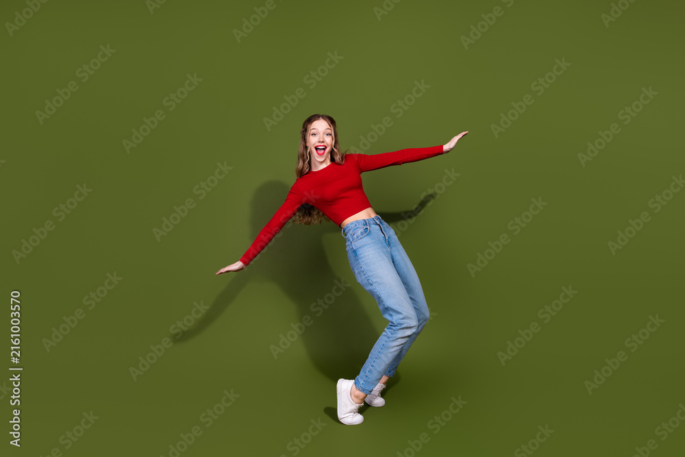 Naklejka premium Energetic young woman in red top and jeans leaps against a green background showing style and joy