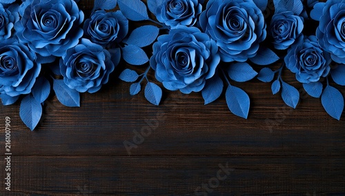 A top-down view of vibrant blue paper roses and leaves against a dark wood background