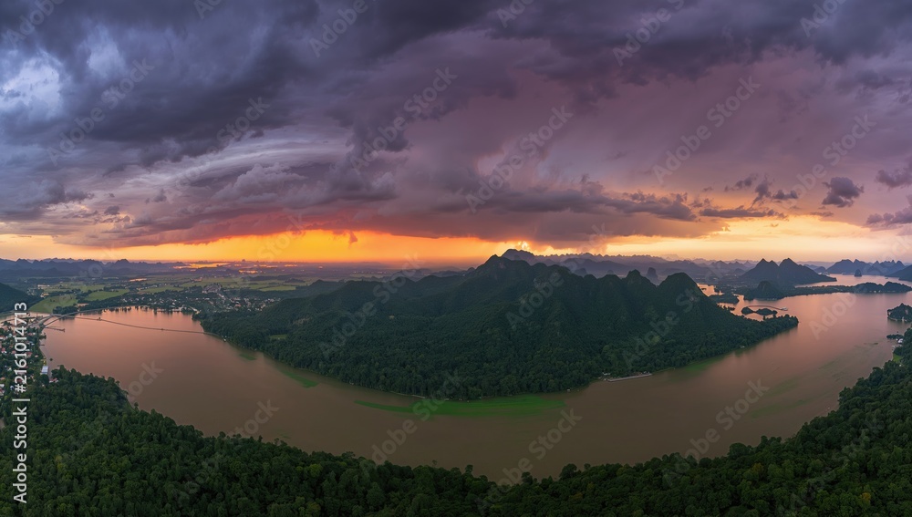 Naklejka premium Majestic Mountain Landscape Overlooking a River at Sunset with Dramatic Clouds