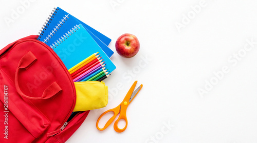 Red backpack with school supplies, apple, and scissors on white background, Back to school concept, copy space