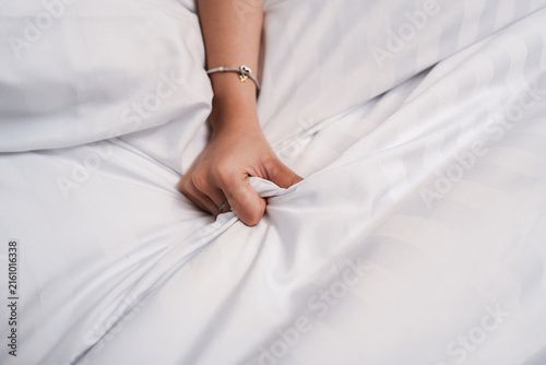 Obraz na płótnie Close up of a woman's hand clenching and gripping the white bed sheet, having sex on bed concept