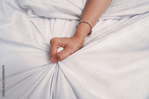 Quadro su tela Close up of a woman's hand clenching and gripping the white bed sheet, having sex on bed concept