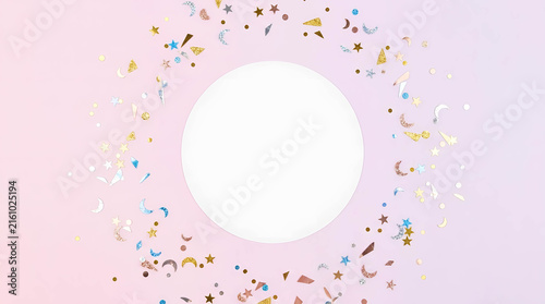 Festive background with empty round paper card surrounded by colorful stars, moon shapes and confetti on pink background