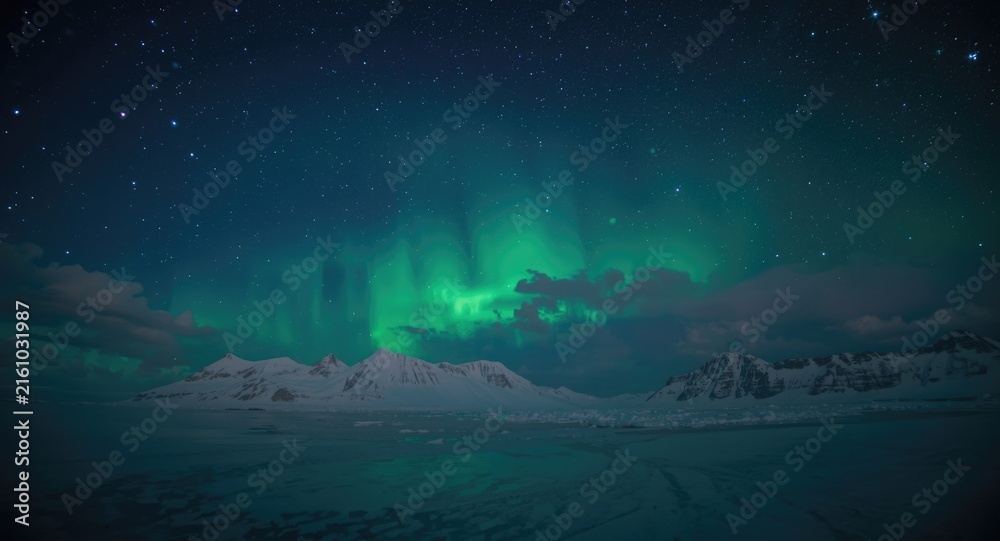 Fototapeta premium Aurora Borealis Illuminating Snowy Mountains Under Starry Sky at Night