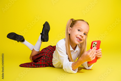 Obraz na płótnie Smiling schoolgirl lying on the floor playing with a smartphone while wearing a