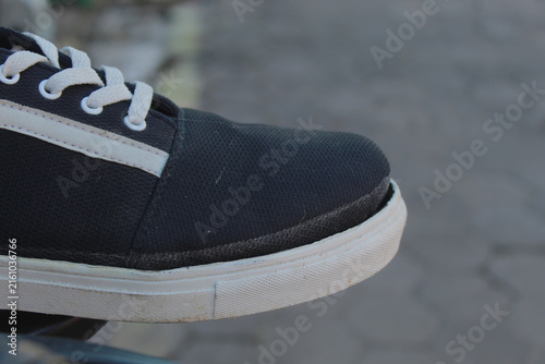 Obraz na plátně A close-up side shot of a dark canvas sneaker showing damage at the toe box where the white rubber sole has separated from the upper material