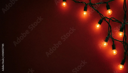 Festive string lights with warm glowing bulbs against a dark red background