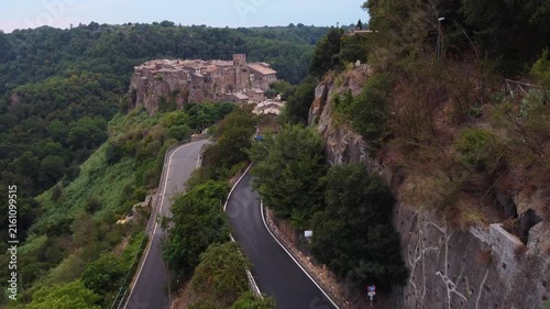 Aerial view of the historic hilltop village of Calcata Vecchia surrounded by lush green forests and winding roads in Calcata Vecchia, Lazio, Italy.