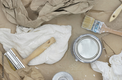 Fotografie Three brushes stained with white paint, old paint in a can, solvent, thinner, cloth, paper towels and brown paper on a beige background, items left over from painting the walls at home