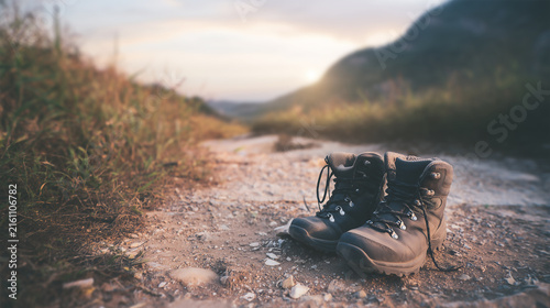 A pair of sturdy hiking boots left on a rough mountain path at sunset, representing travel, adventure, exploration, outdoor activities, freedom, and the journey of a long hike.