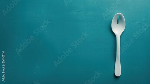 White slotted spoon on teal background.