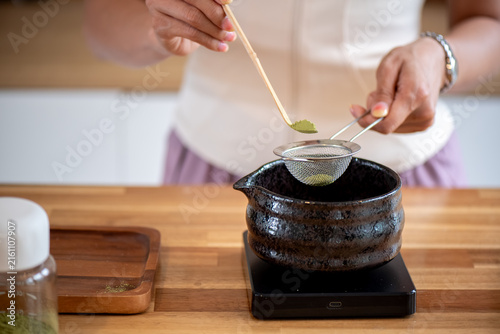 Matcha Preparation – Sifting Green Tea Powder into Ceramic Chawan Bowl on Wooden Table