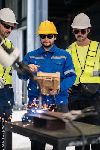 Robotic Welding Team Operating an Automated Robot Arm as Three Workers Observe Bright Sparks on a Metal Worktable in a Factory