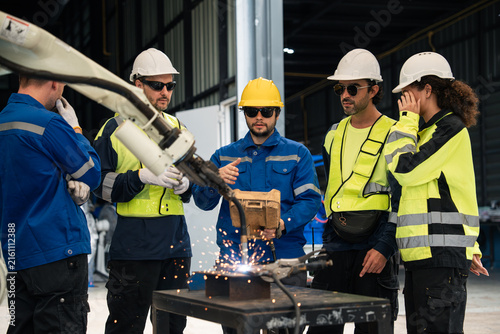 Engineering Team Attending a Robotic Welding Demonstration with Sparks from an Automated Robot Arm in a Manufacturing Workshop