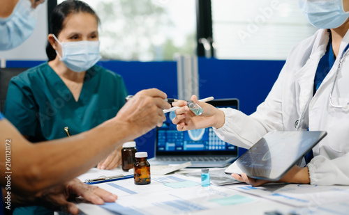 Asian medical team reviews healthcare data, medication samples and digital reports during a clinical meeting, highlighting teamwork, research and medical innovation.