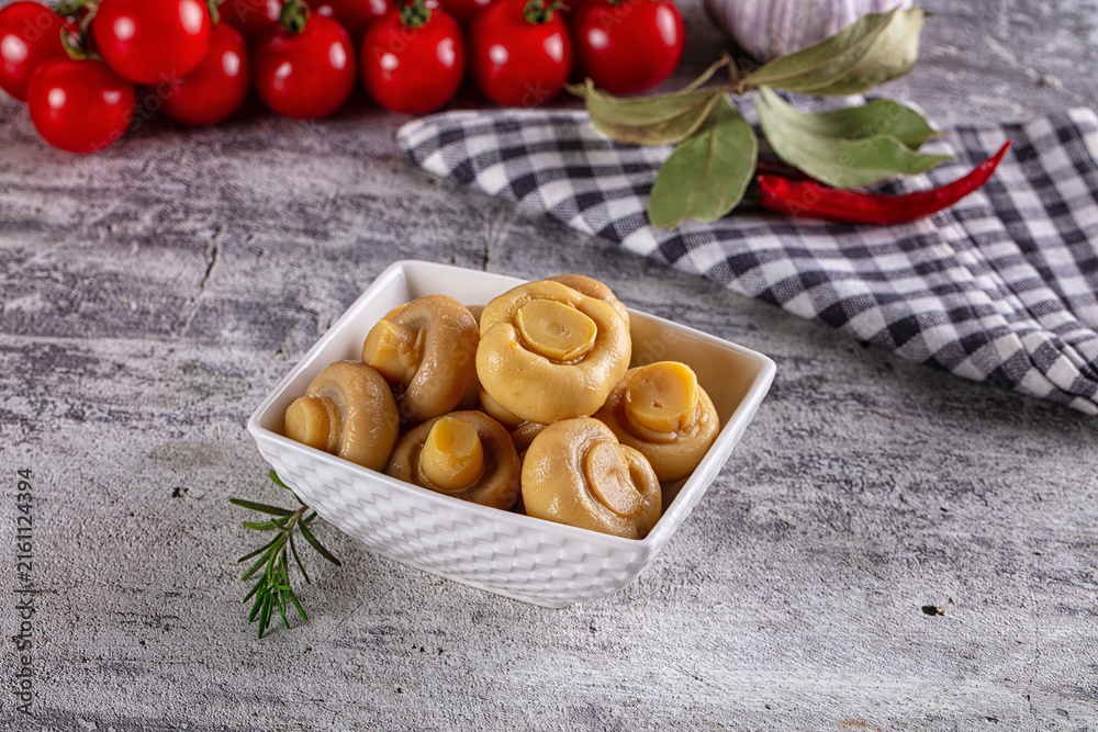 Fototapeta premium Pickled mushrooms in white bowl with cherry tomatoes and herbs on rustic surface