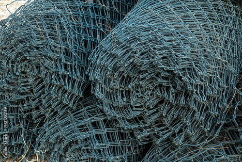 Rolled rolls of dark green woven chain-link wire mesh with mesh texture on construction site.