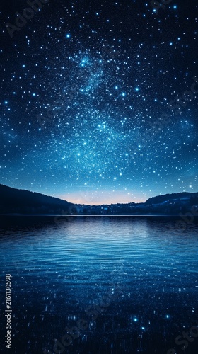 A starry night sky reflects on a calm lake with silhouetted hills in the background.