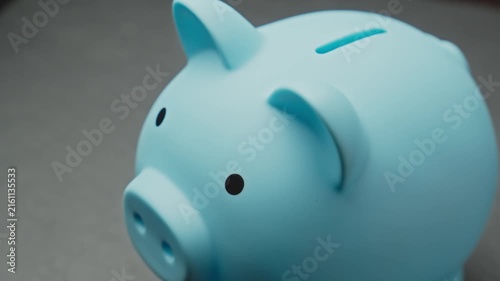 Unrecognizable hand puts coins in blue piggy bank. Save money for your dream. Concept of saving money. Person saves money in piggy bank. Close-up in 4K, UHD