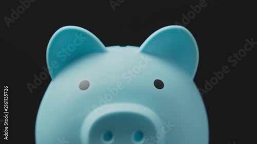 Man putting coins into piggy bank against black background. Piggy bank as concept for storing, accumulating, and saving financial resources. Close-up in 4K, UHD