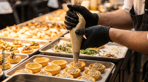 Konstfotografi Chef piping savory truffle cream into mini pastry tartlets for catering