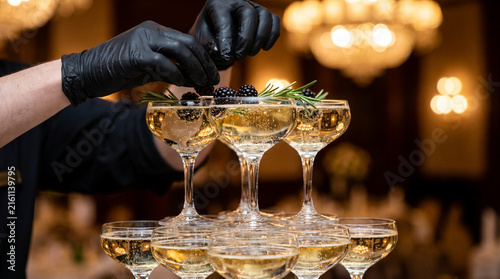 Bartender hands placing fresh blackberries in champagne glass tower for party