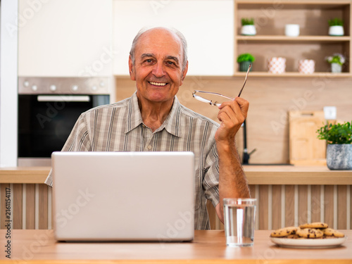 Portrait of senior man working on laptop in comfortable home, showing confidence and satisfaction while staying connected online.