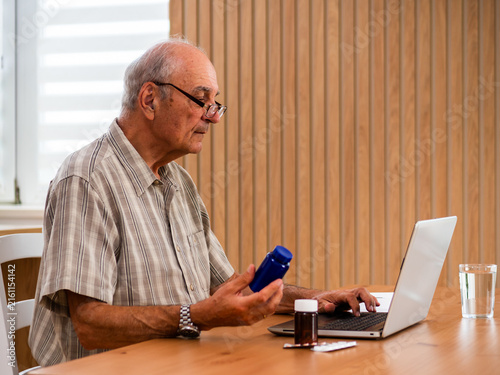 Senior man reading medical advice online while holding pill bottle and using  laptop for remote consultation with his doctor. Copy space for your text or advertisement.	
