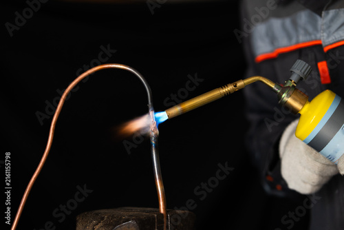 Bild auf Leinwand a worker in protective gloves brazing a copper pipe with a gas torch