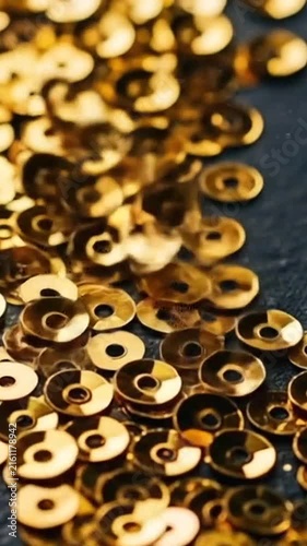 A pile of shiny gold sequins glowing against a dark textured background